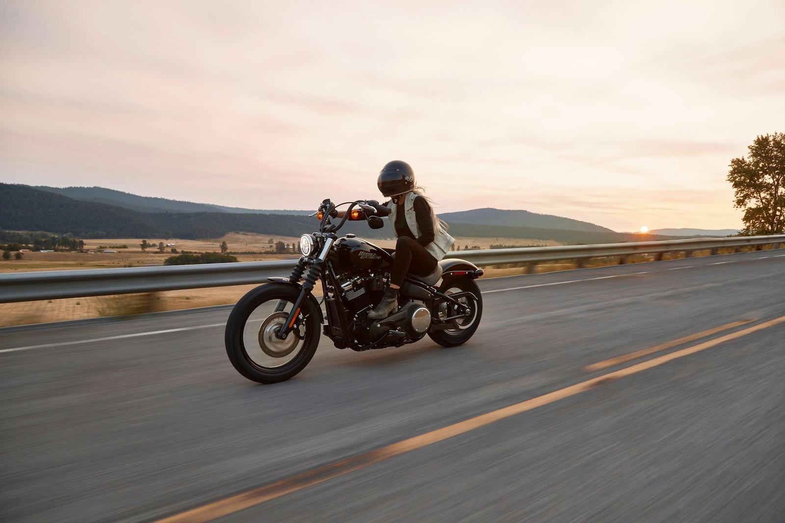 A rider on a cruiser motorcycle on an open road at dusk