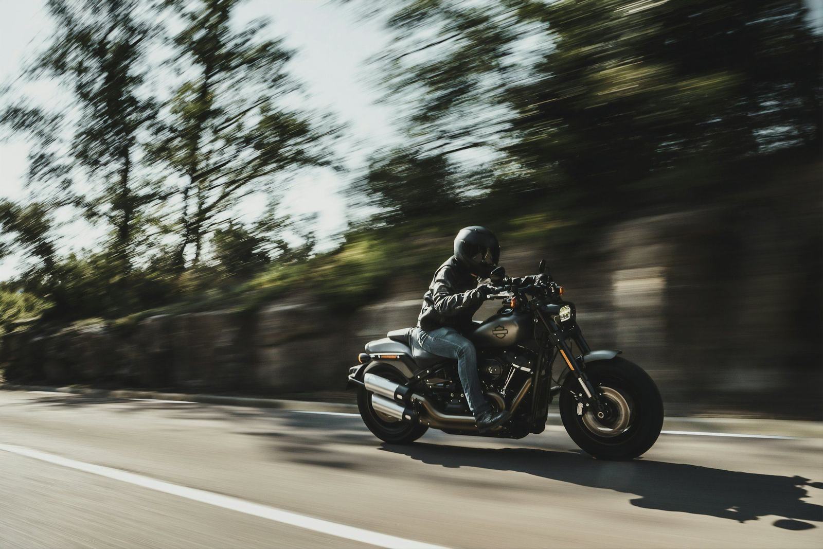 A rider on a cruiser motorcycle moving along a road, the background blurred with speed