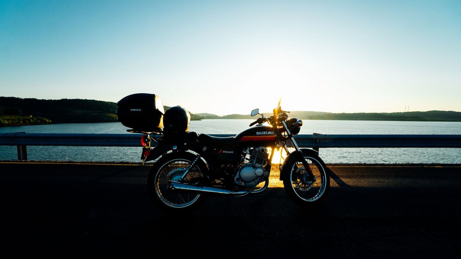 A motorcycle silhouetted beside a lake at sunset