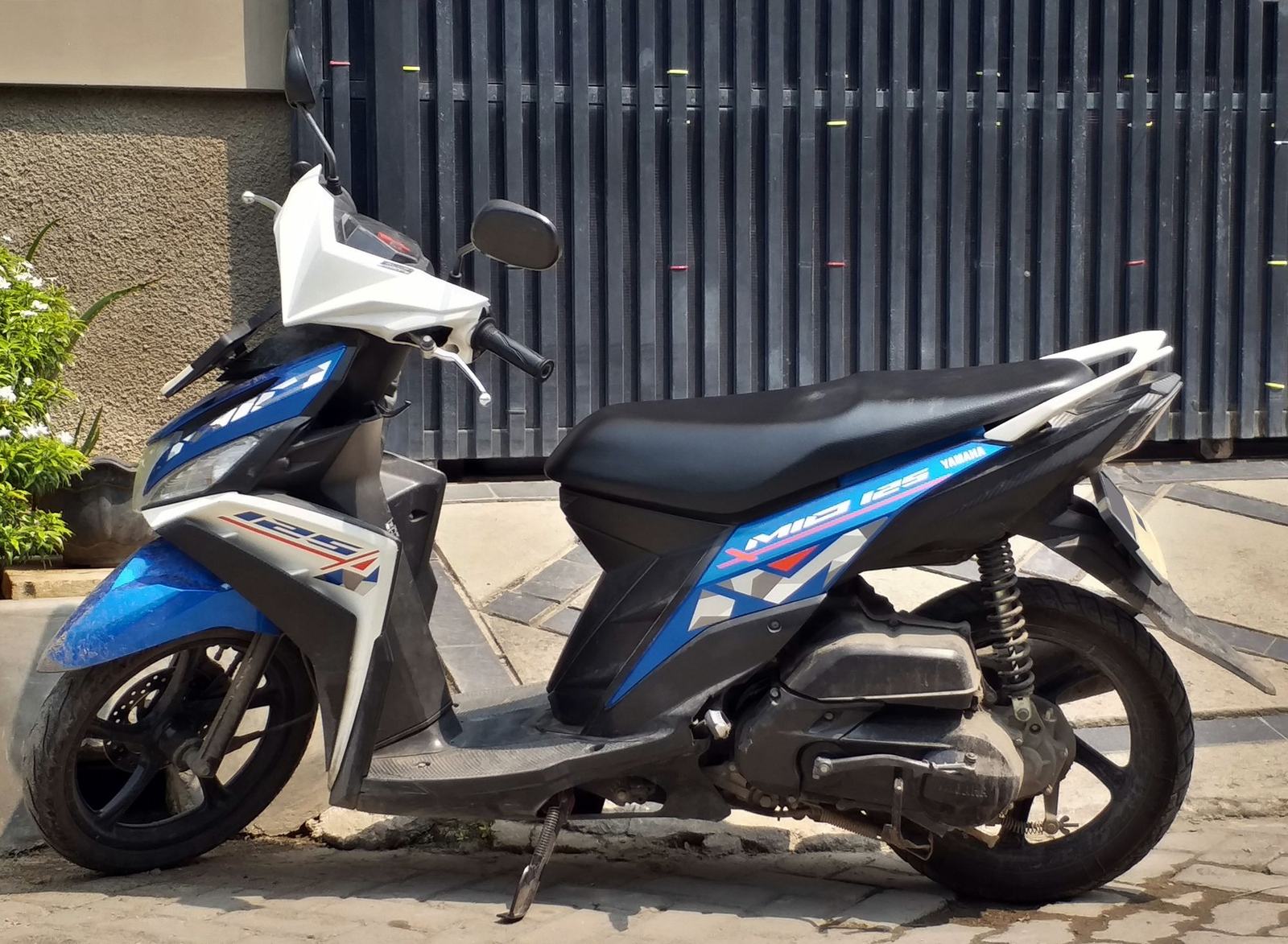 A blue Yamaha Mio M3 125 scooter parked at the kerb, seen from the left side