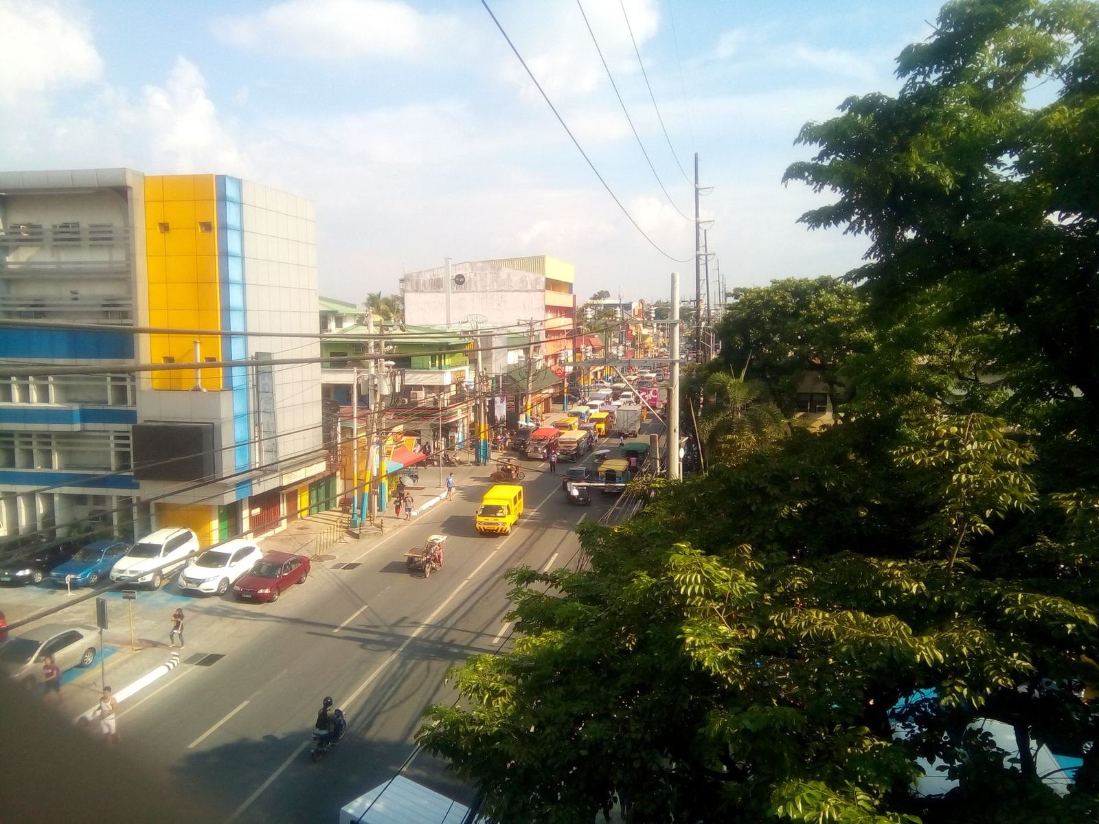 National Road in Muntinlupa seen from an overpass, with jeepneys, tricycles and shops along both sides