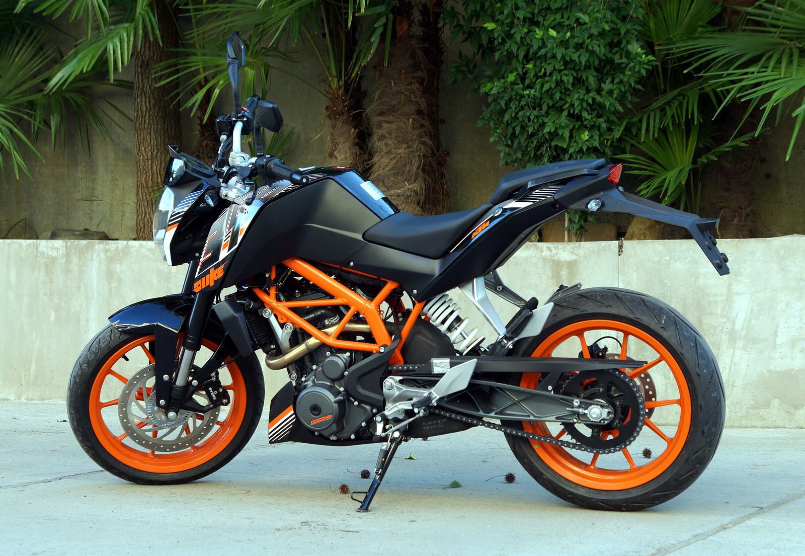 A black KTM 390 Duke with an orange frame and orange wheels, side view, parked in front of palm trees