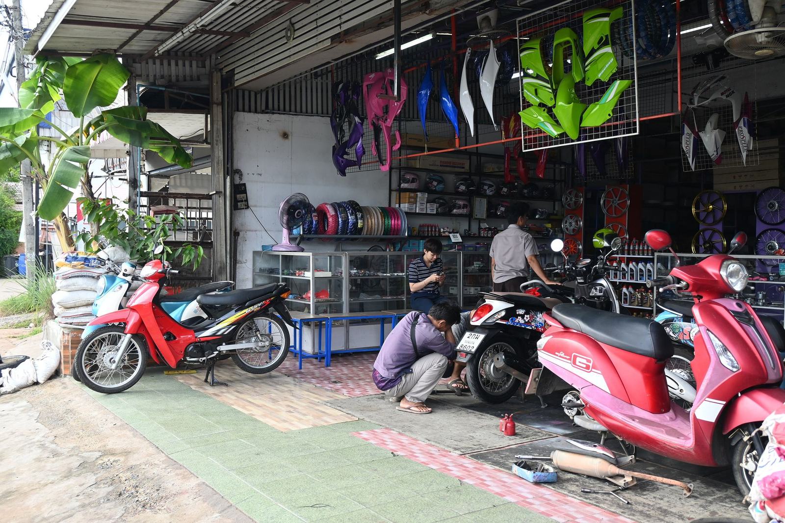 A small motorcycle parts and repair shop with scooters parked in front and fairings hanging inside