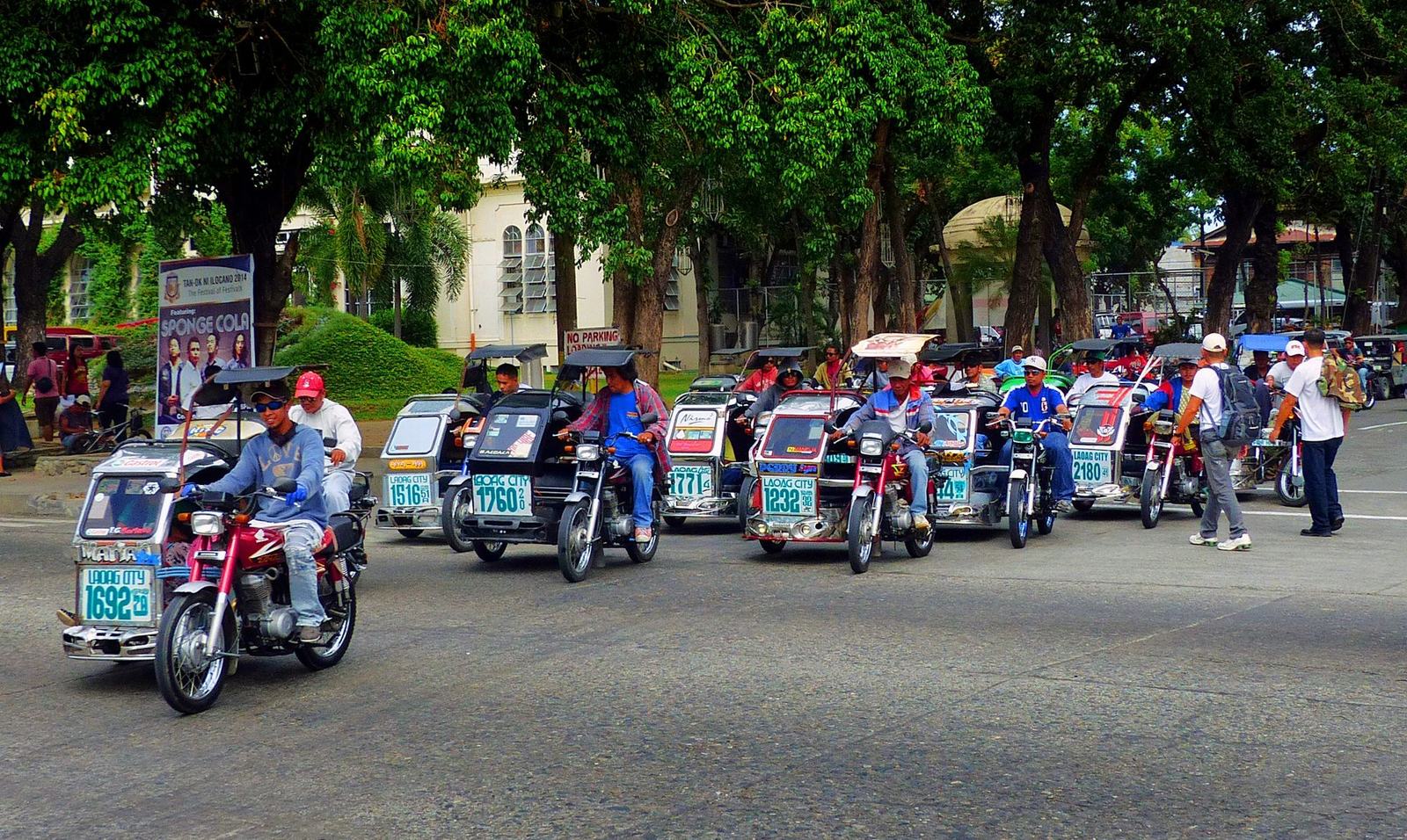 A row of Philippine motorized tricycles parked in a queue, drivers waiting beside them