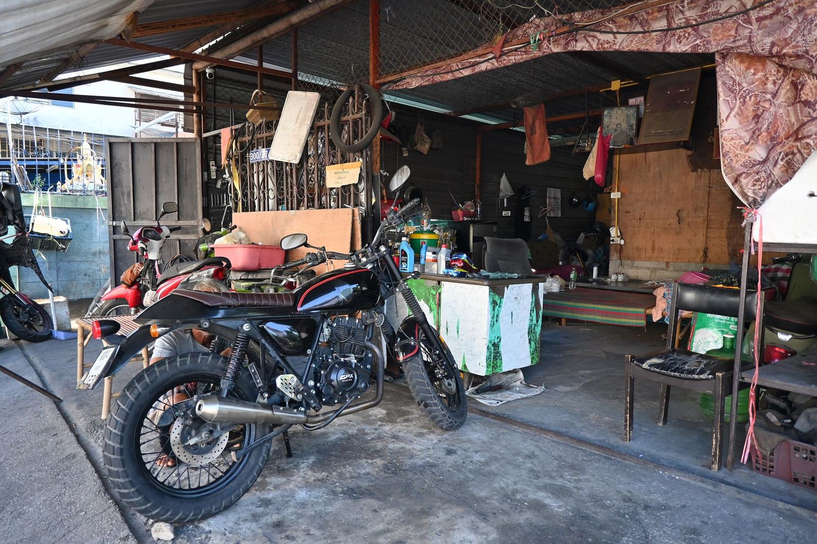 An open motorcycle workshop bay with a bike on the stand and tools along the wall